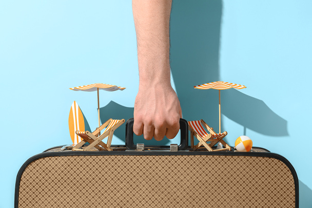 Concept of summer travelling or beach rest. Close up of human hand holds suitcase on a blue background - Photo, Image