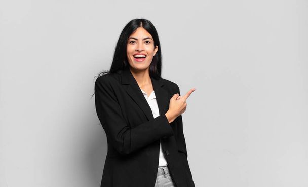 young hispanic businesswoman looking excited and surprised pointing to the side and upwards to copy space - Foto, immagini