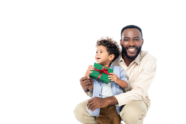 eccitato africano americano uomo sorridente a macchina fotografica vicino bambino ragazzo con regalo isolato su bianco - Foto, immagini