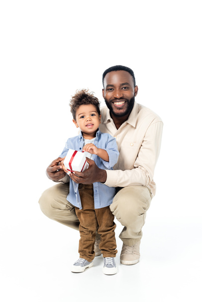 sonriente afroamericano niño sosteniendo presente cerca alegre padre en blanco - Foto, imagen