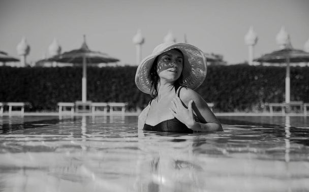 Крупним планом спокуслива дівчина в солом'яному капелюсі купається в басейні. Чорно-біле фото. Відпустка і концепція курорту
. - Фото, зображення