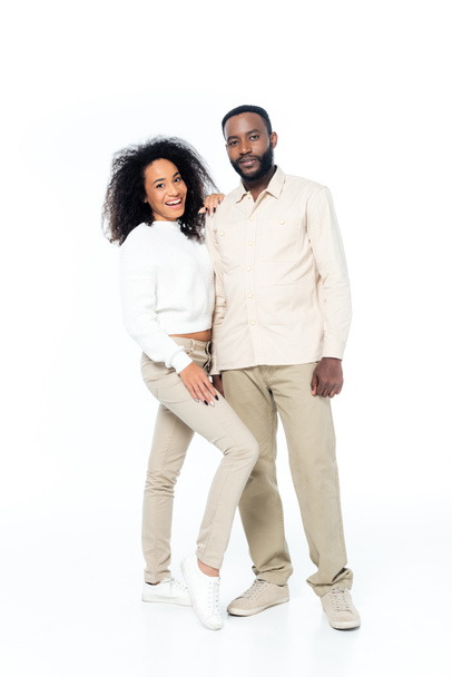 vista completa de la feliz pareja afroamericana sonriendo a la cámara mientras está de pie en blanco - Foto, Imagen