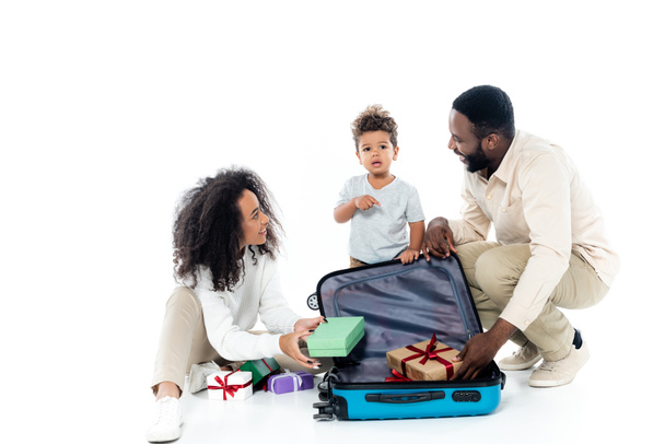 ragazzo africano americano che indica valigia vicino ai genitori felici su bianco - Foto, immagini