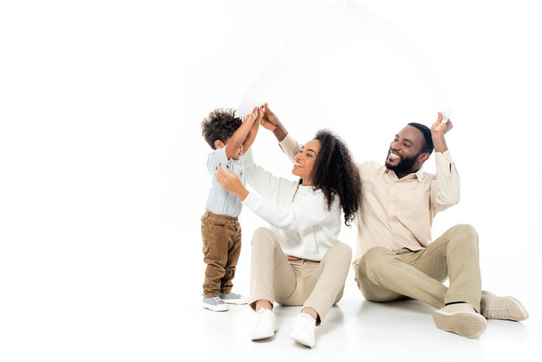 familia afroamericana feliz sosteniendo techo de papel en blanco - Foto, imagen