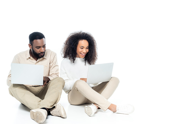 curious african american man looking at laptop in hands of cheerful wife on white - Photo, Image