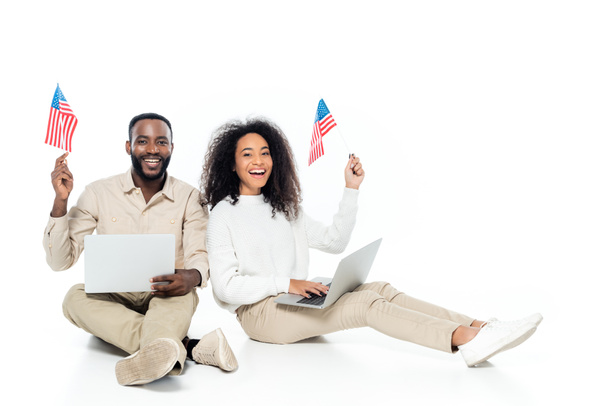 boldog afro-amerikai pár kezében kis zászlók USA miközben ül laptopok fehér - Fotó, kép
