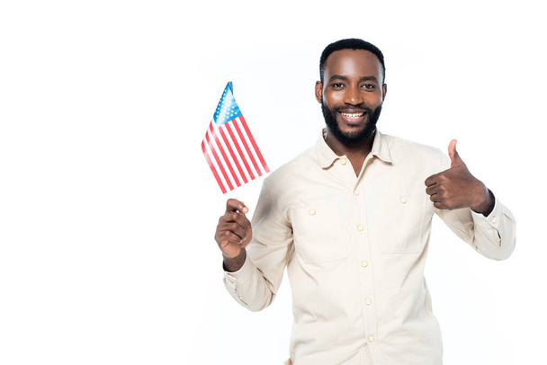 ευτυχισμένος Αμερικανός άνδρας κρατώντας μικρή σημαία των ΗΠΑ, ενώ δείχνει τον αντίχειρα προς τα επάνω απομονώνονται σε λευκό - Φωτογραφία, εικόνα