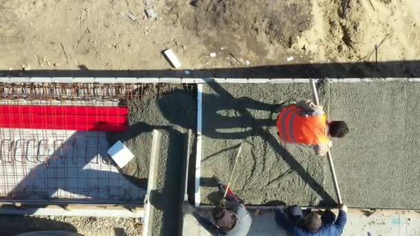 Au-dessus de la vue, les frais généraux sur les travailleurs de la construction se répandent et nivelent le béton frais dans une tranchée carrée après avoir coulé du camion mélangeur sur un pont inachevé. - Séquence, vidéo