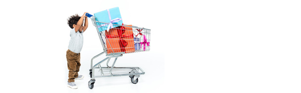 toddler african american boy moving shopping cart with presents on white, banner - Photo, Image