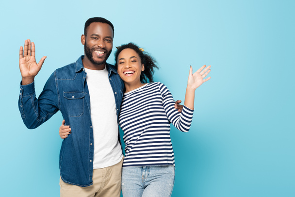 joyeux couple afro-américain agitant les mains à la caméra isolé sur bleu - Photo, image