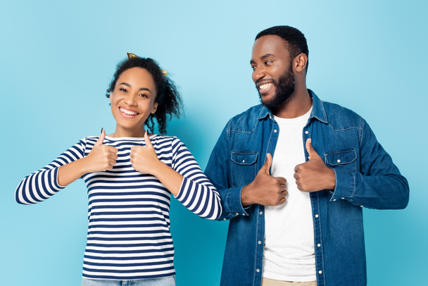 щаслива афро-американська пара посміхається і показує пальці вгору на синьому - Фото, зображення