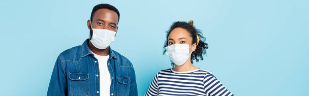 Afrykańska para w maskach medycznych patrząca na odizolowaną na niebiesko kamerę, sztandar - Zdjęcie, obraz