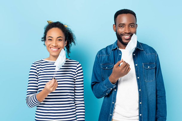 щаслива подружня пара афроамериканців, що знімає маску для медиків на синьому - Фото, зображення