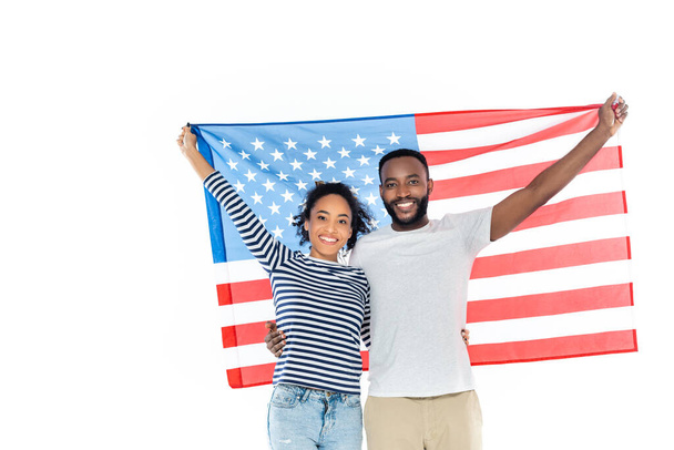 Neşeli Afro-Amerikan çifti beyaz kameraya bakarken ABD bayrağını tutuyor. - Fotoğraf, Görsel
