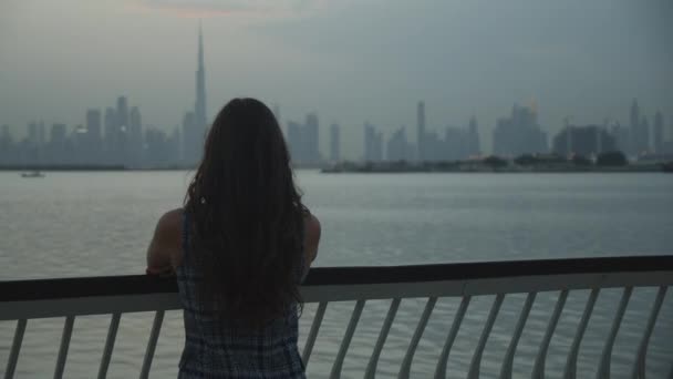 Femme regardant les gratte-ciel de Dubaï à travers l'eau. Tourisme profitant du paysage urbain de Dubaï avec de grands gratte-ciel en soirée - Séquence, vidéo