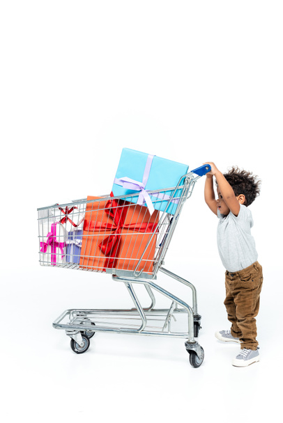 pieni afrikkalainen amerikkalainen lapsi liikkuvat ostoskorissa lahjapakkaukset valkoinen - Valokuva, kuva