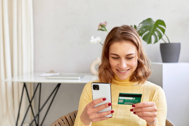 Улыбающаяся женщина, платящая картой за онлайн покупку по телефону - Фото, изображение