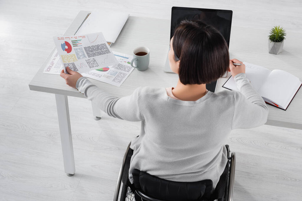 Yleisnäkymä vammaisten freelancer työskentelevät paperit lähellä kannettavaa tietokonetta ja cup pöydällä  - Valokuva, kuva