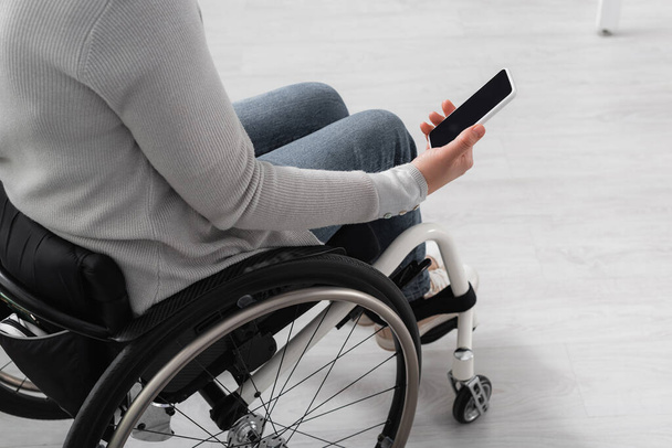 Oříznutý pohled na zdravotně postiženou ženu na invalidním vozíku drží smartphone s prázdnou obrazovkou doma  - Fotografie, Obrázek