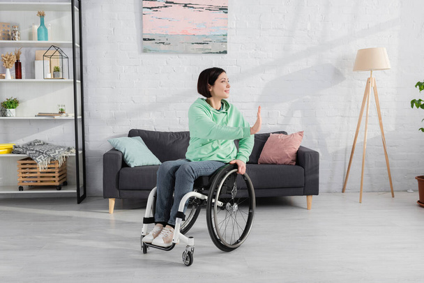 Usmívající se žena na invalidním vozíku cvičení v blízkosti gauč doma  - Fotografie, Obrázek