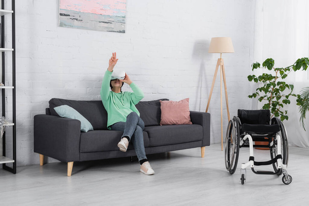 Γυναίκα παίζει βιντεοπαιχνίδι σε vr ακουστικά κοντά σε αναπηρική καρέκλα στο σπίτι  - Φωτογραφία, εικόνα