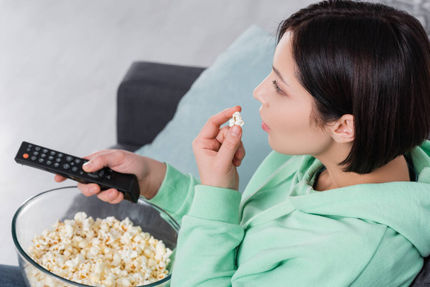 Brünette Frau mit Fernbedienung hält Popcorn  - Foto, Bild