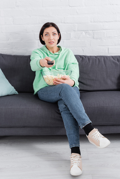 Mujer con mando a distancia y palomitas de maíz sentado en el sofá  - Foto, Imagen