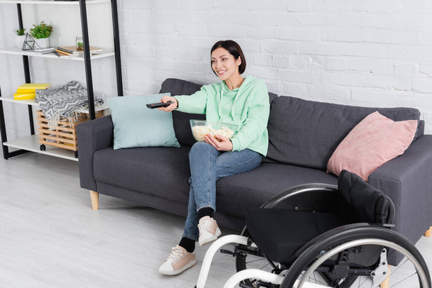 Mulher feliz com pipocas assistindo filme perto de cadeira de rodas em primeiro plano borrado  - Foto, Imagem