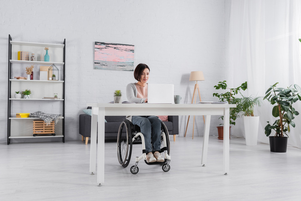 Libero professionista disabili utilizzando computer portatile vicino a carte e tazza in soggiorno  - Foto, immagini