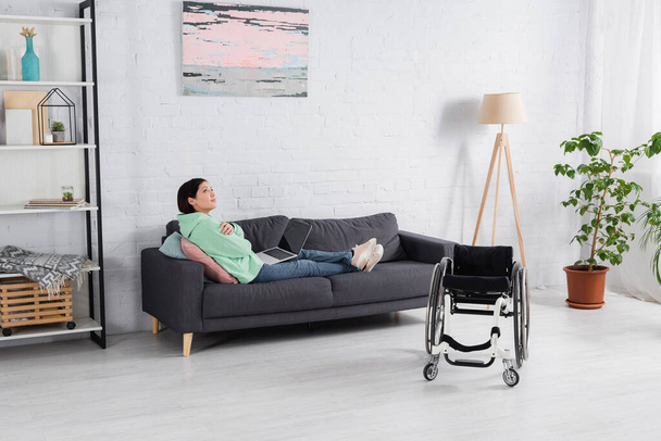 Фрілансер з вимкненим ноутбуком, що сидить на дивані біля інвалідного візка
  - Фото, зображення
