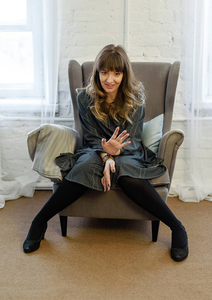 Emozionale bella giovane bruna seduta su una sedia in soggiorno a casa - Foto, immagini