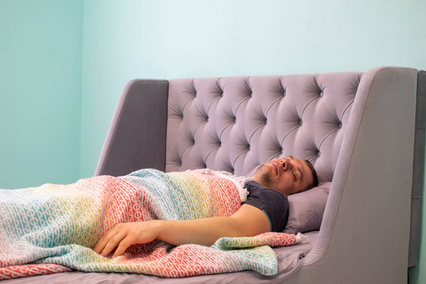 男は横になり、枕でベッドの上で寝ています。健康的な姿勢の概念。男は多色のプレイの下にある. - 写真・画像