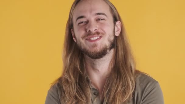 Joven hombre rubio de pelo largo sonriendo en la cámara sobre el fondo colorido. Muchacho barbudo atractivo buscando feliz - Imágenes, Vídeo