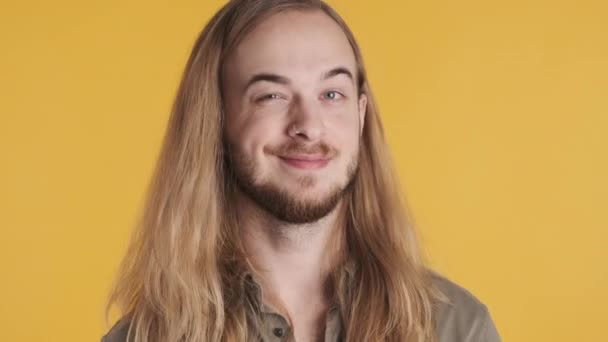 Giovane uomo biondo dai capelli lunghi strizzando l'occhio sulla macchina fotografica e sorridendo su sfondo giallo - Filmati, video