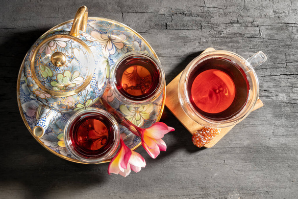 Coupe en verre de thé fraîchement infusé avec Plumeria fleur, bâton de sucre de cannelle et bouilloire traditionnelle sur table en bois sombre, top vie - Photo, image