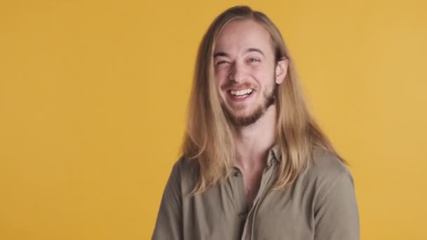 Allegro ragazzo biondo dai capelli lunghi che sembra felice ridendo sulla macchina fotografica su sfondo giallo - Filmati, video