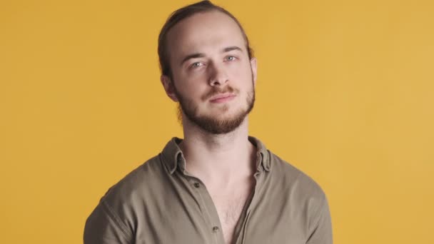 Młody, atrakcyjny brodaty mężczyzna ubrany w luźne ubranie, wyglądający pewnie przed kamerą na żółtym tle. Wyraz twarzy - Materiał filmowy, wideo