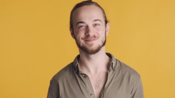 Jonge aantrekkelijke bebaarde man die er vrolijk lachend en zwaaiend hallo op camera over gele achtergrond uitziet. Groet uitdrukking - Video
