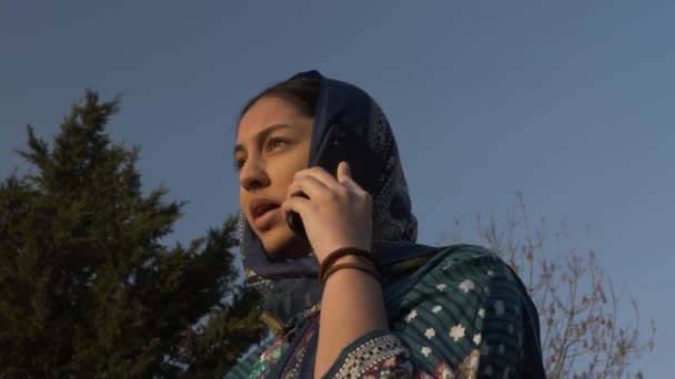 ゴールデンアワーに携帯電話で話す若いムスリム女性10代。低角度、ロックオフ - 映像、動画