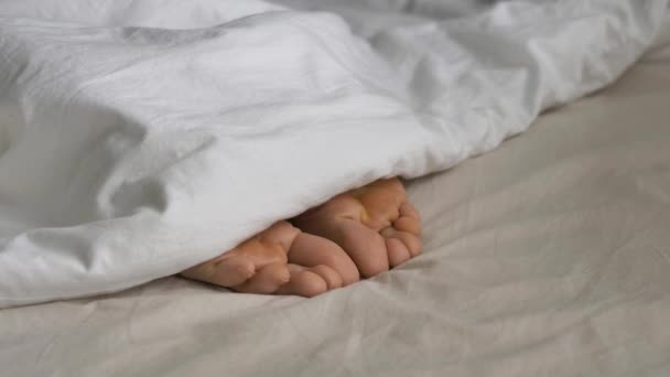 Unelias henkilö peitetty huopa kiemurtelee varpaat sängyssä - Materiaali, video