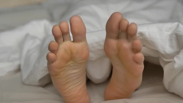 Joven con edredón suave retuerce los dedos de los pies descansando en la cama - Metraje, vídeo