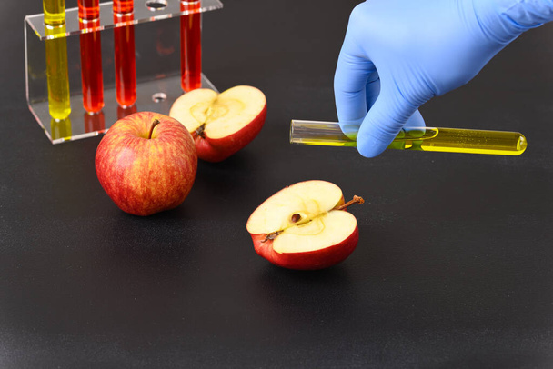 Piros alma és laboratóriumi üveg sárga folyadékkal. A gyümölcs színe. - Fotó, kép