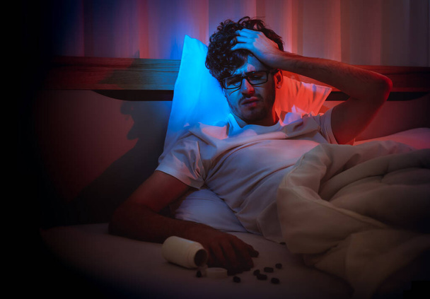Przygnębiony bezsenność biały człowiek trzymając głowę na łóżku późno w nocy z Black Medical pigułki na stres i koncepcja samobójstwa. - Zdjęcie, obraz