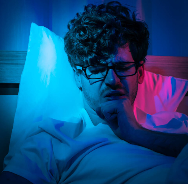 Безсоння безсоння чоловік має проблеми зі сном вночі з будильником, який розповідає вночі на своєму ліжку
. - Фото, зображення