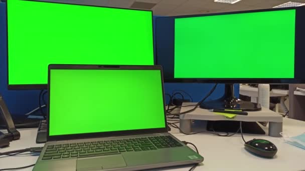 Workstation of 3 computer monitor on desk with green screen in 4k. One laptop connected with 2 monitors as extended display in an office enviornment - Footage, Video