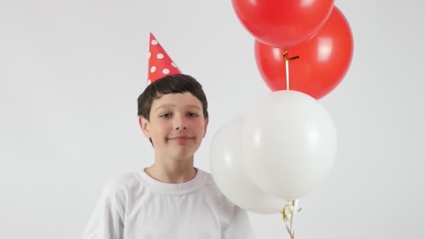 Cumpleaños. Retrato de un niño riendo con un sombrero rojo de cumpleaños. Bolas rojas y blancas.  - Metraje, vídeo