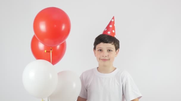 Γενέθλια. Μπαλόνια. Όμορφο αγόρι με κόκκινο καπέλο γενεθλίων. Κόκκινα και άσπρα μπαλάκια. 4K - Πλάνα, βίντεο
