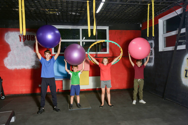 Kinder halten Fitnessbälle in der Turnhalle hoch. - Foto, Bild