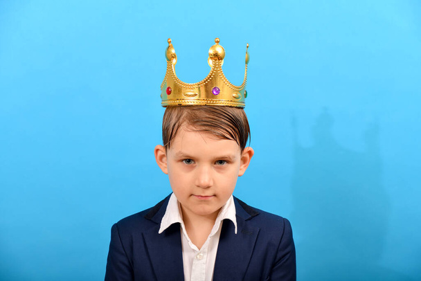 Rapaz de fato e com uma coroa de ouro na cabeça num fundo azul. dominação e poder sobre os outros. - Foto, Imagem