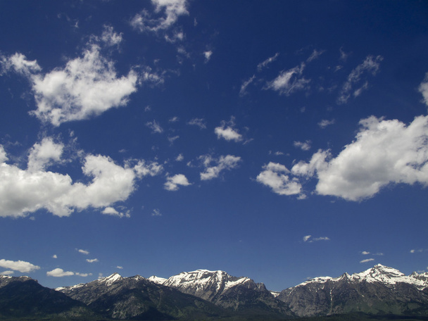 Pörröiset pilvet hallitsevat kirkasta sinistä taivasta, jonka alla on lumihuippuiset Grand Teton vuoret. Voidaan käyttää tausta edustaa mitä tahansa vuorijono
. - Valokuva, kuva